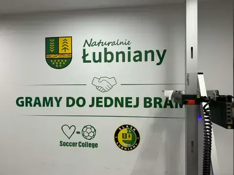 Ściana z grafiką Naturalnie Łubniany, herbem gminy oraz logotypami klubu Śląsk Łubniany