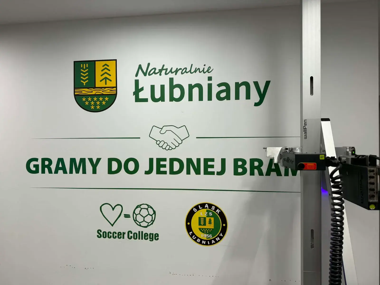 Ściana z grafiką Naturalnie Łubniany, herbem gminy oraz logotypami klubu Śląsk Łubniany — zdjęcie 1 z 3